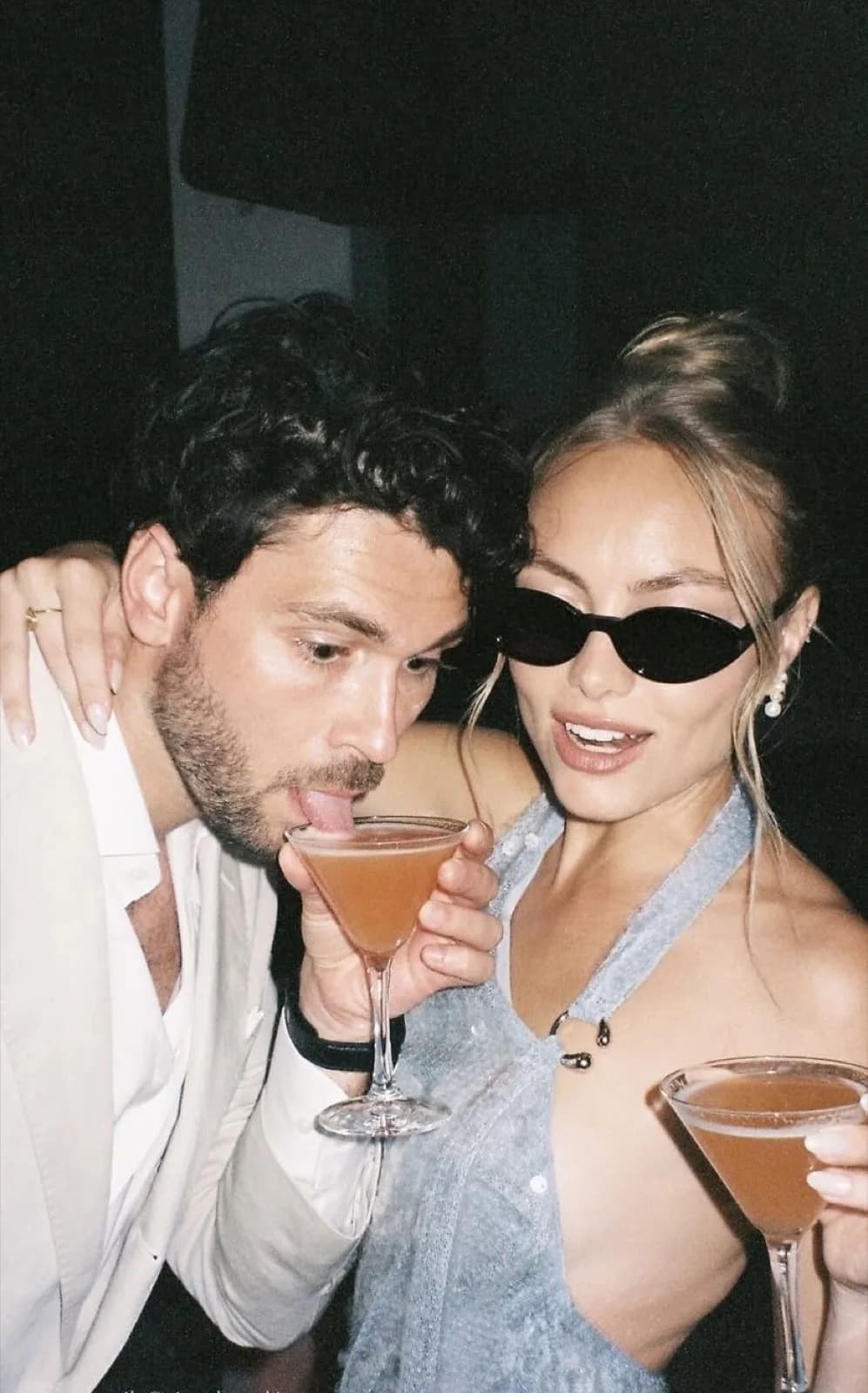 A couple caught by the flash, two cocktail glasses raised late in the night