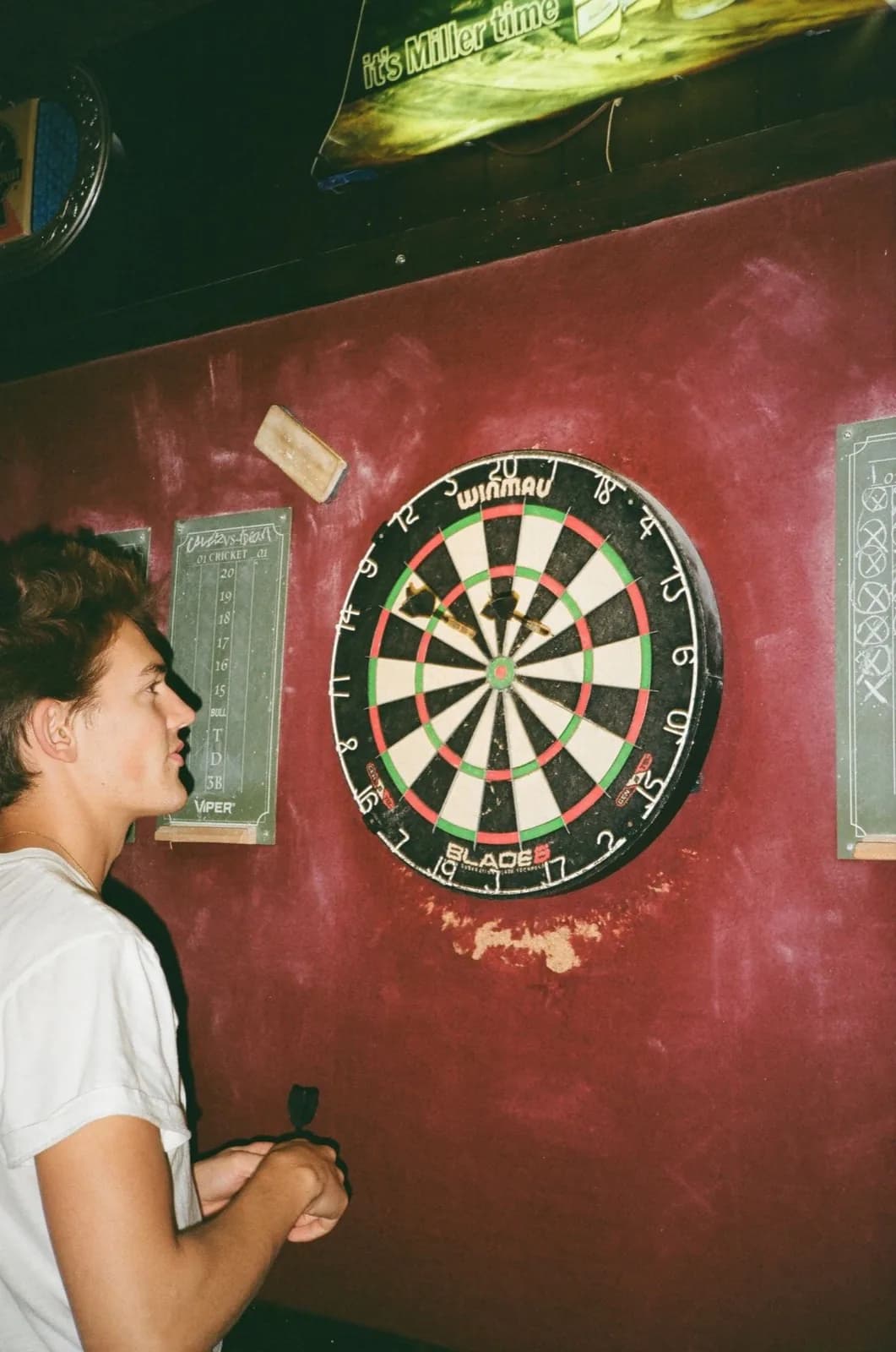 Darts player lining up his throw in a burgundy-painted bar, shot on film
